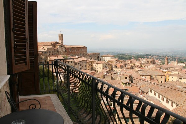 A balcony with a view of a historic town, featuring terracotta-roofed buildings and a prominent church tower.
