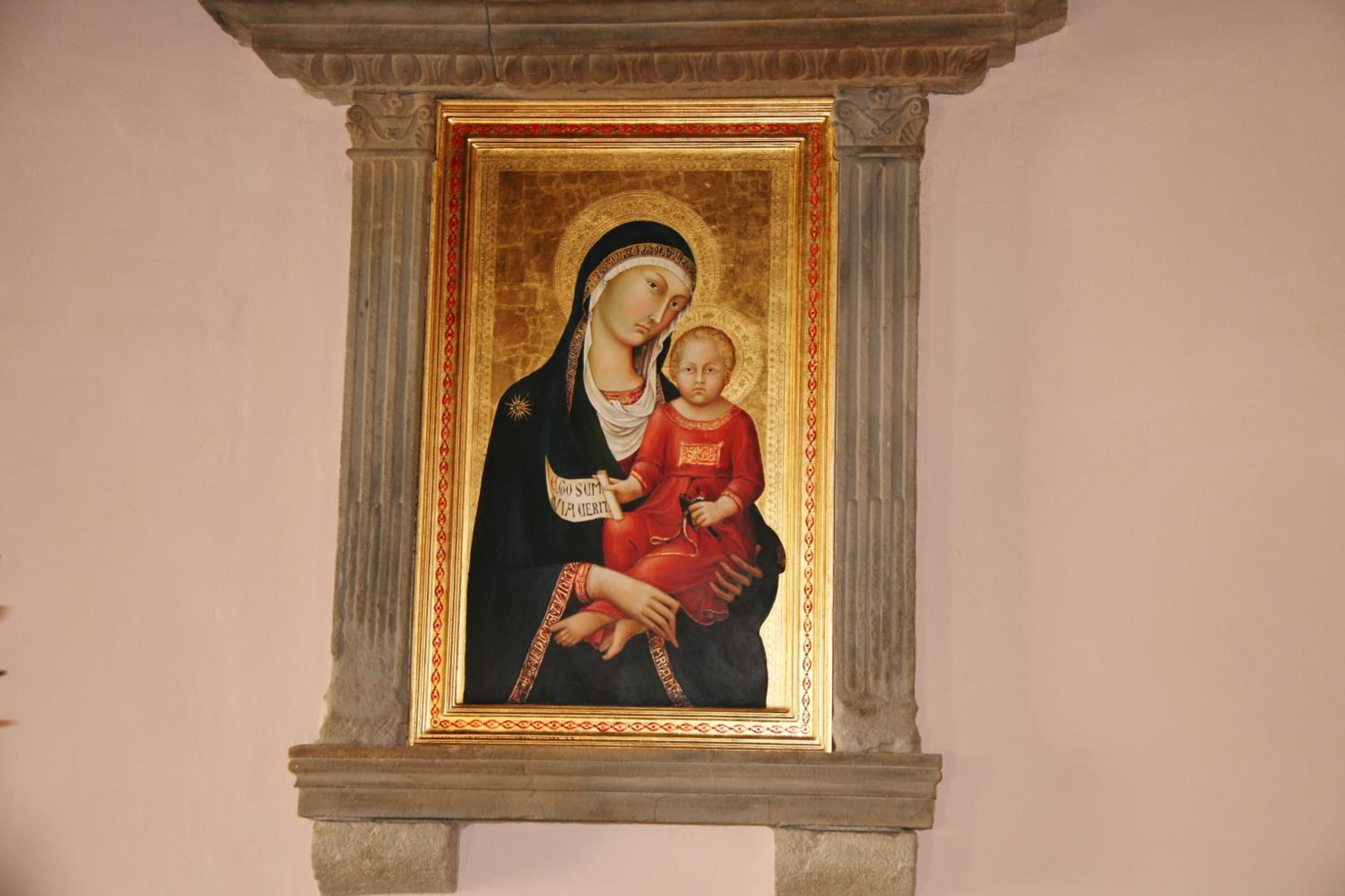 Un tableau religieux encadré, doté d’un cadre doré, fixé sur une structure en pierre.