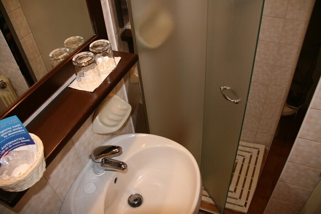 Un bany amb un rentamics blanc, un mirall i una cabina de dutxa de vidre.