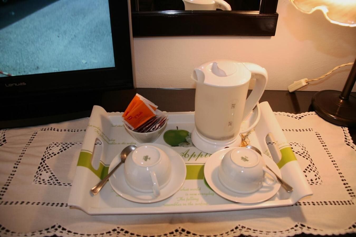 A tray with a teapot, cups, a bowl of tea bags, and a spoon on a table with a doily.