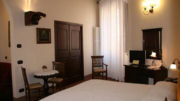 Une chambre d’hôtel avec un grand lit, un bureau avec un ordinateur, une chaise, une petite table avec un vase et une grande fenêtre avec des rideaux.