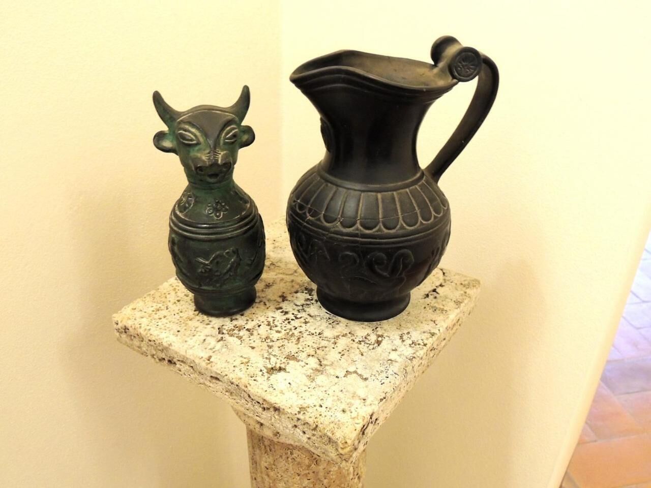 Deux objets en céramique, posés sur un piédestal en pierre, devant un mur uni.