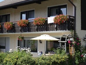 A two-story building with balconies adorned with flower boxes and an outdoor seating area with an umbrella. - Double room 4 - Erd's Hoimatle (Jungholz)