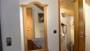 Une chambre avec une porte en bois, un lit, un miroir et une salle de bain avec douche.