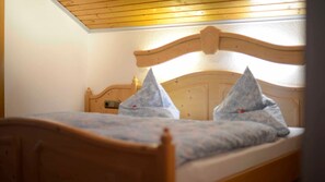 A single bed with a wooden headboard and two pillows, a wooden ceiling, and a white wall. - Double room 4 - Erd's Hoimatle (Jungholz)