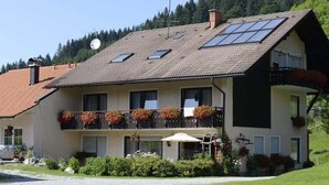 Un bâtiment à deux étages, doté d’un toit en pente, de nombreuses fenêtres et d’un balcon orné de plantes en pot.