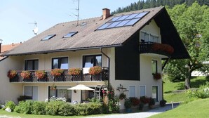 Une maison à deux étages, dotée d’un toit en pente, de panneaux solaires et d’un balcon agrémenté de jardinières.