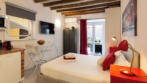 A bedroom with a bed, a desk, a chair, a TV, and a balcony with red curtains.