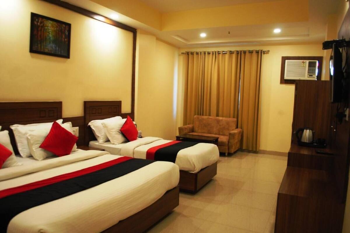 A hotel room with two beds, a sofa, a chair, an air conditioning unit, and a painting on the wall.