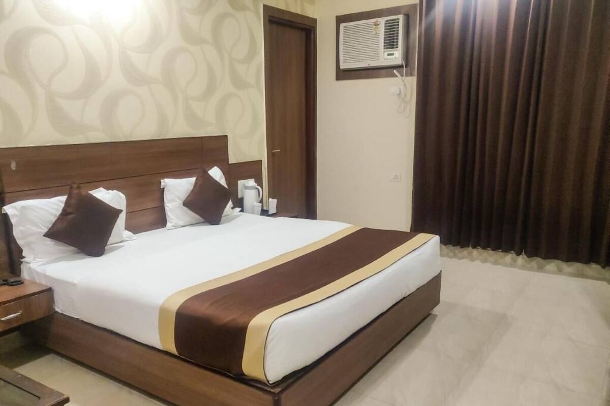A hotel room with a large bed, a wooden headboard, a nightstand, a bedside table, and a wall-mounted air conditioning unit.