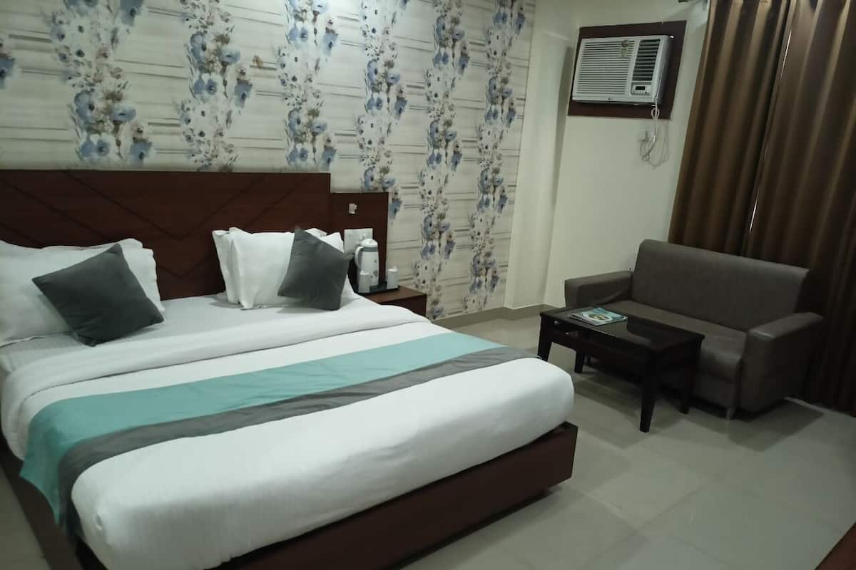 A hotel room with a large bed, a sofa, a coffee table, and a wall-mounted air conditioner.