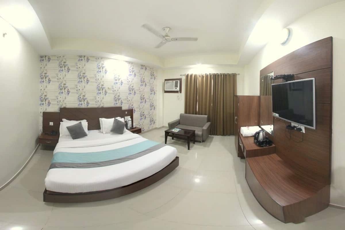 A hotel room with a bed, a TV, a desk, a chair, a ceiling fan, and a window with curtains.