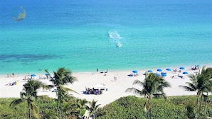 A beach with clear turquoise water, palm trees, and people sunbathing.