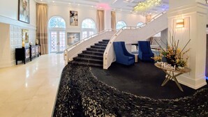 A grand lobby with a marble floor, a staircase, and a reception desk.