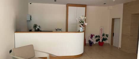 Un área de recepción con mostrador, zona de estar y una planta en maceta.