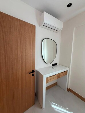 A room with a wooden door, a white vanity with a mirror, and an air conditioning unit mounted on the wall. - Pasahan Apart (Marmaris)