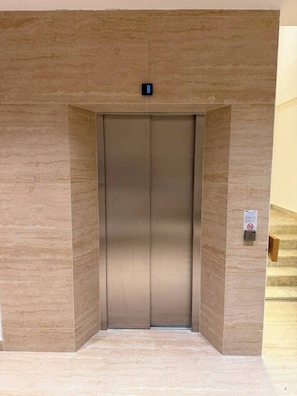 A modern elevator with a digital display above the door, a safety sign on the wall, and a staircase to the right. - Pasahan Apart (Marmaris)