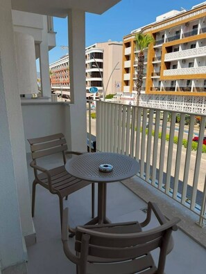 A balcony with two chairs and a round table, overlooking a street with buildings and a palm tree. - Pasahan Apart (Marmaris)