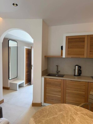 A modern kitchen with wooden cabinets, a sink, and a coffee maker. There is a bench in the hallway leading to a door. - Pasahan Apart (Marmaris)