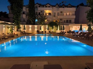 A swimming pool with lounge chairs and umbrellas, surrounded by buildings with balconies. - Pasahan Apart (Marmaris)