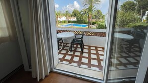 Un balcon donnant sur une piscine, des palmiers et un sol carrelé.