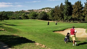 Un parcours de golf avec un chemin bien défini, un bunker de sable et une ville située au loin.