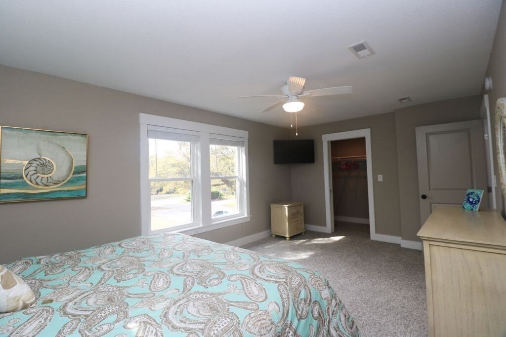 A bedroom with a bed, a ceiling fan, a TV, a closet, and a window.