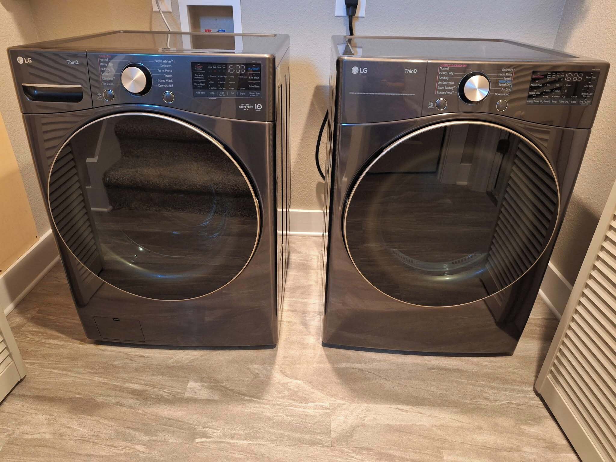 Two LG ThinQ front-loading washing machines in a laundry room with a tiled floor and a white wall.
