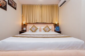 A neatly made bed with white bedding and two decorative pillows, a bedside table with a lamp, and a wall-mounted air conditioner. - Hotel Axis International (Mumbai)