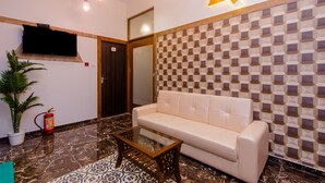 A modern lobby with a white sofa, a glass coffee table, a patterned floor, a fire extinguisher, and a mounted television. - Hotel Axis International (Mumbai)
