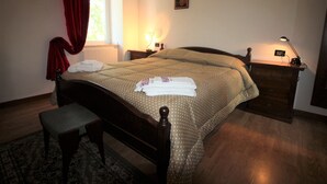 Un letto rifatto con copriletto a pois, una panca in legno, un comodino con una lampada e una finestra con tende rosse.