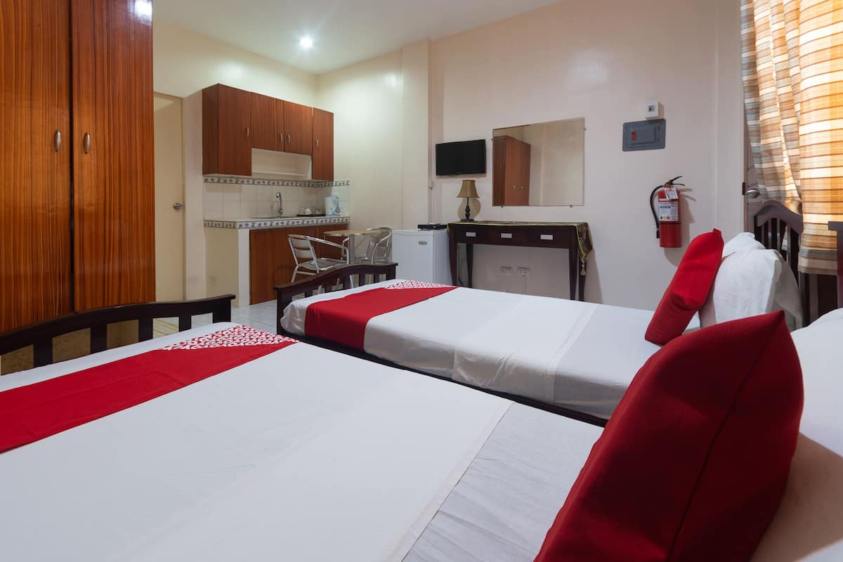 Camera d'albergo con due letti, una scrivania, una sedia, un angolo cottura e una TV, oltre a un estintore.