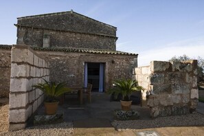 Un edificio rustico in pietra con tetto in tegole, una porta in legno e piante in vasi nel cortile.