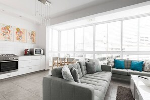 A modern kitchen with white cabinets, a grey sofa, and a dining area with a white table and chairs.