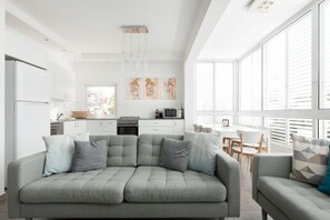 Una cucina moderna con mobili bianchi, un'area pranzo con tavolo e sedie, e un divano grigio con cuscini.