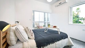A bedroom with a bed, bedside lamp, window, and a small table with a plant. - Beachside Apartment: Modern Comfort & Style (Tel Aviv-Yafo)