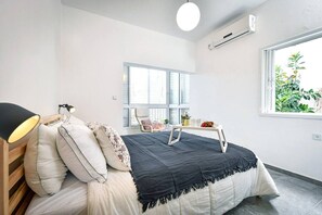 Una camera da letto con un letto, una lampada da comodino, una finestra e un tavolino con una pianta.
