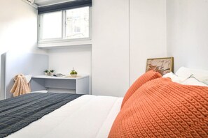 A bedroom with a bed, a desk, a window, and a picture frame.
