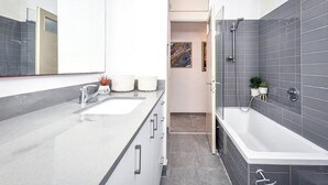 A modern bathroom with a large bathtub, a separate shower area, and a vanity with a sink. - Beachside Apartment: Modern Comfort & Style (Tel Aviv-Yafo)