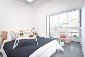 A bedroom with a bed, bedside table, lamp, chair, and large windows.