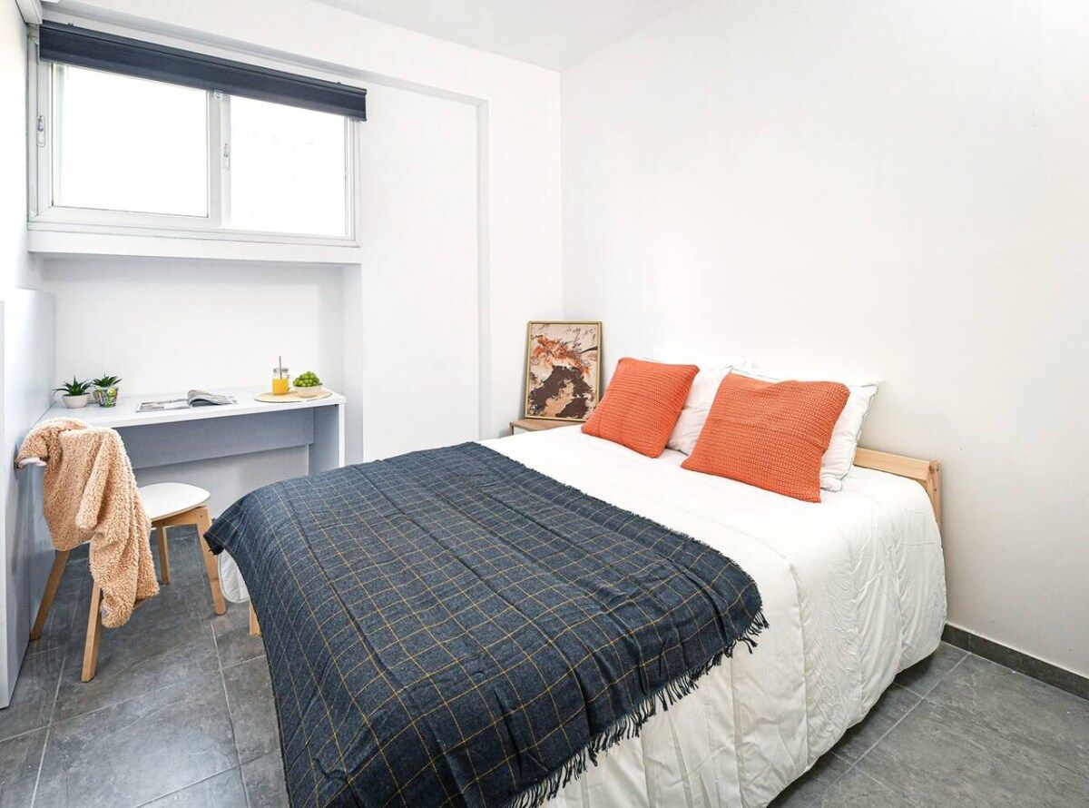 Une chambre à coucher avec un lit, un bureau, une chaise et une fenêtre.