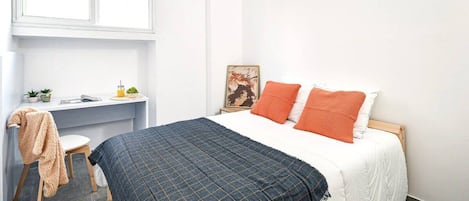 Un dormitorio con cama, escritorio, silla y ventana.