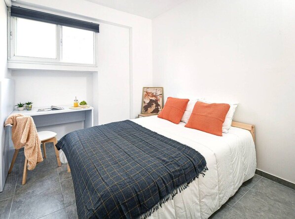 A bedroom with a bed, a desk, a chair, and a window.