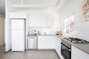 A modern kitchen with white cabinetry, a dishwasher, a stove, and a window with blinds.
