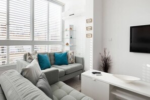 A modern living room with a grey sofa, a white console table, and a large window with blinds.