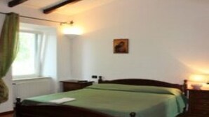 Ein Schlafzimmer mit Bett, Nachttisch, Lampe und einem Fenster mit Vorhängen.