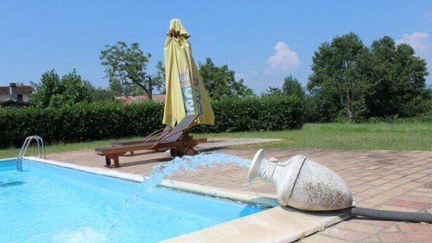 Ein Schwimmbecken mit einer Fontäne, einer Bank und einem Sonnenschirm.