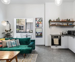 A compact living space with a green sofa, a small dining table, and a kitchenette.