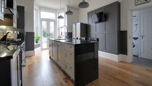 A modern kitchen with a central island, built-in appliances, and a large window providing natural light. - Belmont Road (Broadstairs)