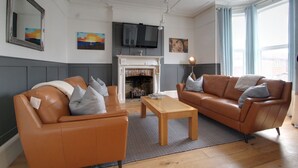 A living room with two leather sofas, a wooden coffee table, a fireplace, and a television mounted above it. - Belmont Road (Broadstairs)
